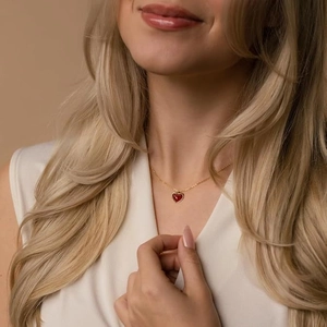 Close-up of minimalist heart necklace with red pendant and gold chain on model