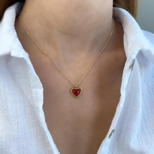 Minimalist gold necklace with deep red heart pendant worn on white textured shirt