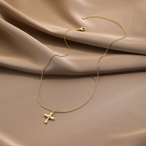 Detailed close-up of a golden cross pendant on a silk fabric with adjustable chain clasp