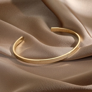 Detail view of 14k gold plated C-shaped open cuff bracelet on elegant champagne silk fabric