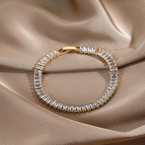 Detail of 14k gold plated tennis bracelet with baguette cut stones on champagne silk fabric