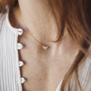 Close-up of a sparkling 18K gold heart pendant necklace with zircon pavé on a model neck