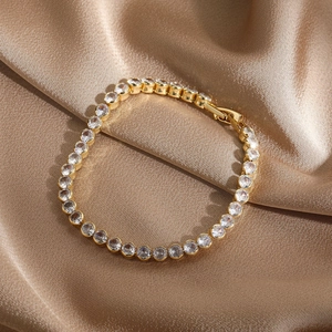 Detail of 14k gold plated tennis bracelet with sparkling zircons on champagne silk