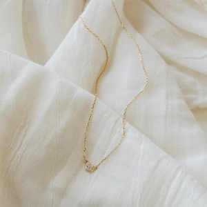 Macro shot of minimalist gold heart necklace with white zircon pavé on white linen