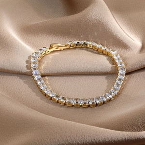 Detail of 14k gold plated tennis bracelet with square-cut zircons on champagne silk