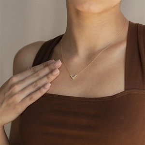 Macro shot of gold V-shaped pendant necklace with cubic zirconia on female model