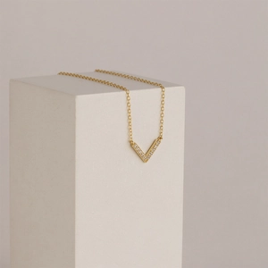 Macro shot of V-shaped gold pendant with cubic zirconia on white geometric stone