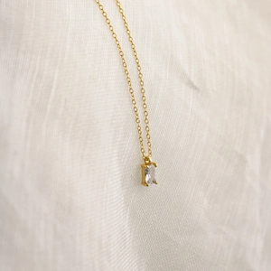 Detailed close-up of emerald-cut zircon pendant with four-prong setting on gold chain