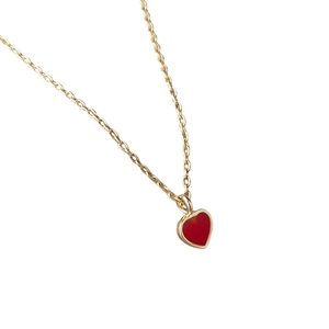 Close-up of a delicate gold chain necklace featuring a glossy red heart enamel pendant