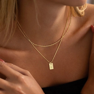 Dettaglio di una collana dorata a due strati con catena satellite e pendente rettangolare 'E'