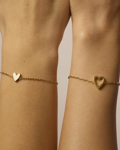 Dettaglio di bracciali in oro minimalisti con ciondoli a cuore indossati al polso