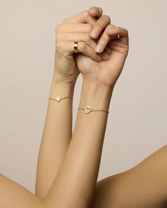 Dettaglio di braccialetti dorati con cuore minimalista e anello a strati sul polso