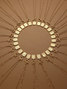 Collectie gouden vierkante alfabet hangers met OT-sluiting op een bruine ondergrond