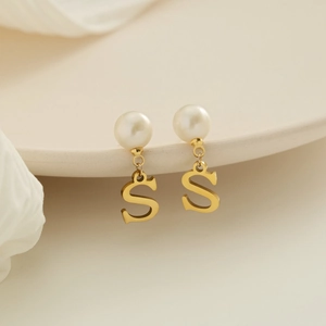 Eleganti orecchini dorati con perle bianche e ciondolo lettera S su vassoio in ceramica