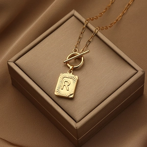 Gouden ketting met letter R hanger en OT-sluiting op zijdeachtige stof getoond