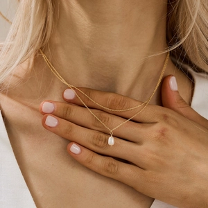 Close-up of double-layer gold chain necklace featuring a glossy white pearl pendant