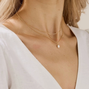 Double-layered gold chain necklace with pearl pendant on model neck and collarbone