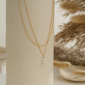 Detail of a minimalist double-layer gold chain necklace with a natural pearl pendant