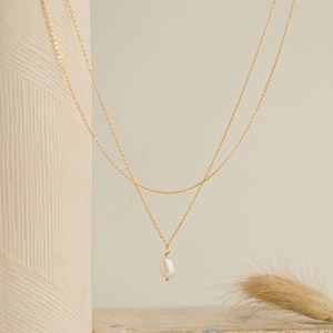 Elegant double-layered gold chain necklace with baroque pearl pendant on ceramic decor