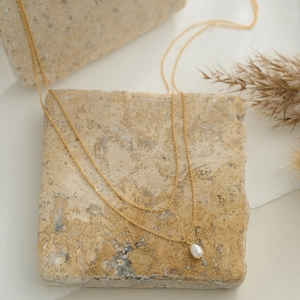 Detail of a minimalist gold double-layer necklace with a white teardrop pearl pendant