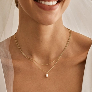Close-up of double-layer gold necklace featuring a radiant white teardrop pearl pendant