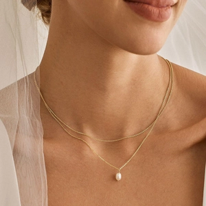 Detail shot of elegant double-layered gold necklace with water-drop pearl on model skin