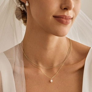 Close-up of double-layer gold necklace with pearl pendant on model with bridal veil