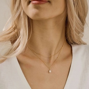 Close-up of double-layered gold necklace with a teardrop pearl pendant on a model