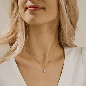 Elegant double-layered gold necklace with a white pearl pendant shown on a model