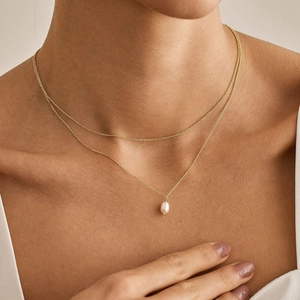 Dettaglio di un set di collane dorate a due strati con un pendente di perla luminosa