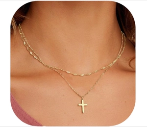 Close-up of a double-layered gold cross necklace with twisted chain on a model's neck