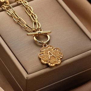Macro detail of golden paperclip chain necklace with initial A clover pendant and OT buckle