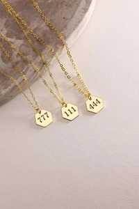 Macro detail of three gold hexagon angel number pendants with 777 111 444 engravings