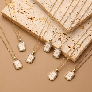 Detail view of gold square letter pendants with white shell inlay and zircon border