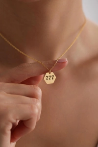 Detail of gold hexagon pendant featuring engraved angel number 777 on a dainty chain