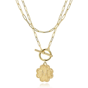 Close-up of double-layer gold necklace featuring a letter M clover pendant and toggle clasp