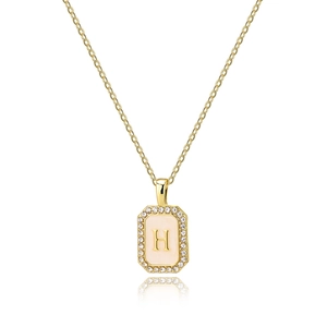 Macro detail of golden rectangular pendant with letter H and white zircon stones