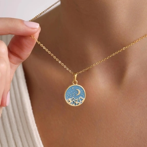 Detail of gold necklace with blue enamel star and moon landscape pendant on skin