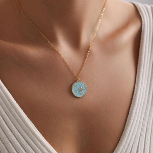 Close-up of gold necklace with blue star pendant worn by a model in a white shirt