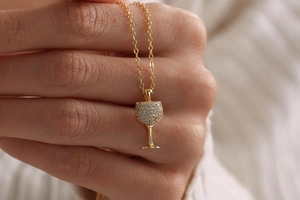 Close-up of golden necklace featuring a crystal-encrusted wine glass shaped pendant detail