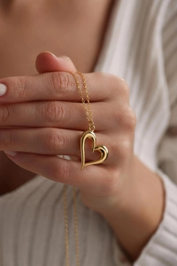 Detail of hand holding a polished gold hollow heart pendant on a delicate chain