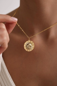 Close-up of a 18K gold sun medallion pendant worn on a minimalist delicate chain