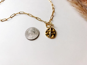 Detail of gold paperclip chain necklace featuring a hammered cross pendant and toggle clasp