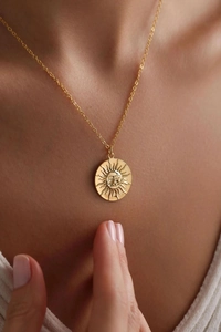Close-up of a gold sunburst medallion necklace worn by a model in soft lighting