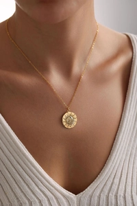 Close-up of golden sun medallion necklace worn with white V-neck knitted top
