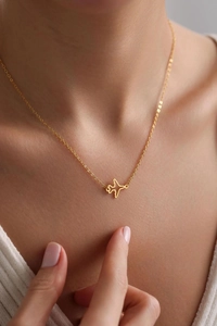 Detail of a minimalist gold plane pendant necklace worn on a female neck with white sweater