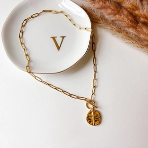 Gold paperclip chain necklace with a cross pendant and toggle clasp on a white tray
