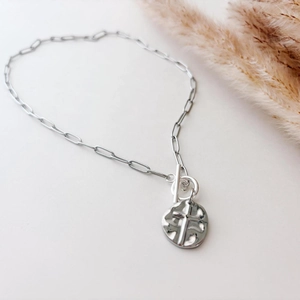 Silver paperclip chain necklace with cross pendant and OT clasp on a minimal background