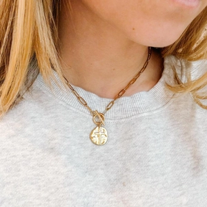 Gold paperclip chain necklace with a cross disc pendant and toggle clasp on a model