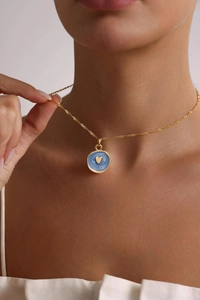 Close-up of golden heart medal necklace with blue pearl enamel on a female model